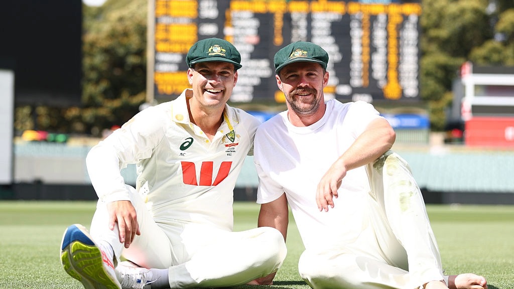Alex Carey and Travis Head sit on the outfield, in front of the scoreboard, at the Adelaide Oval after scoring centuries for Australia against England in the 3rd Test of the Ashes 2025/26