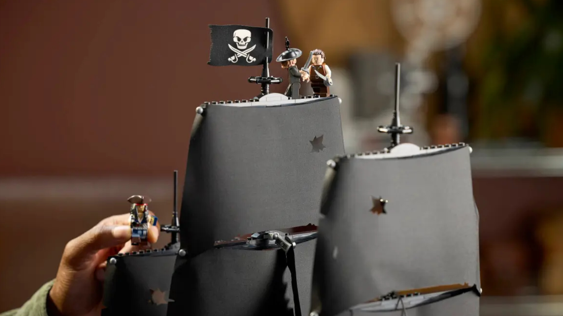 Lego Barbossa and Will minifigures battle atop the mast, with a hand placing Jack below them