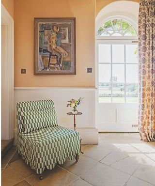 green checked accent chair in corner of room with peach coloured walls and arched glass doorway and stone floors and artwork on wall