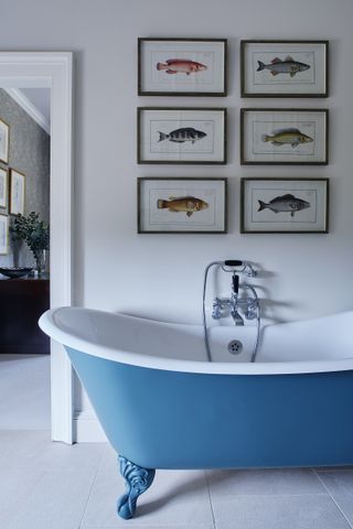 bathroom with blue painted bath and fish artworks on wall