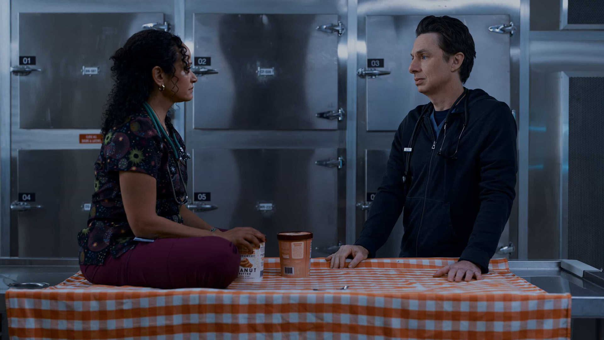 كارلا تجلس متربعة على طاولة يقف بجانبها JD في Scrubs الموسم 10 الحلقة 7