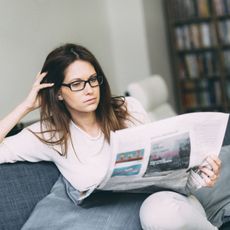 Woman sitting on couch reading newspaper