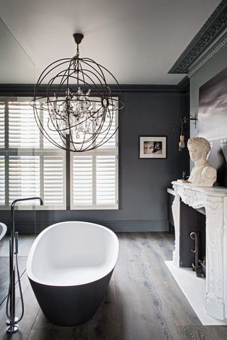 dark grey bathroom with freestanding bath, white fire place and statement pendant light