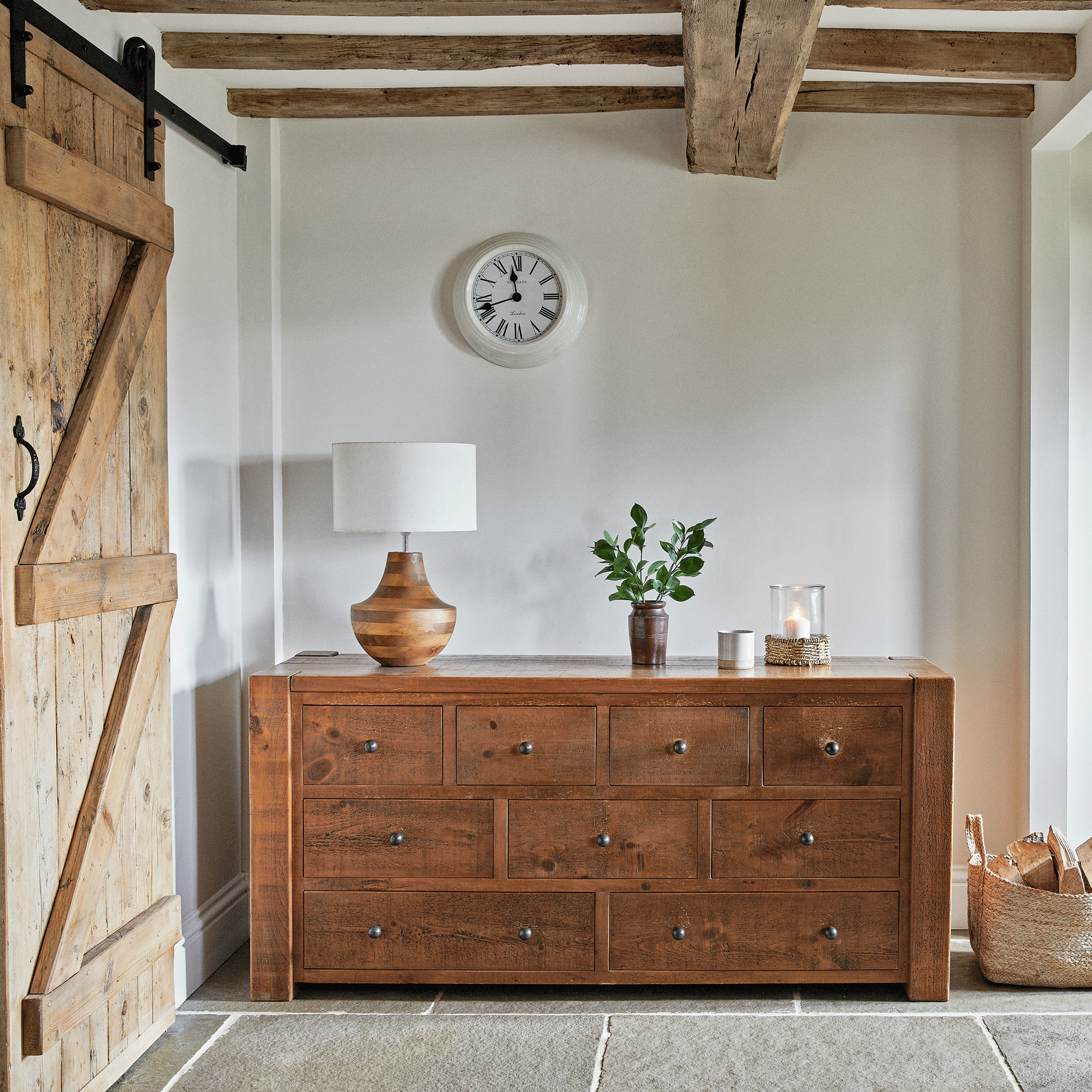 a hallway with a chest of drawers, a lamp, clock and vase on top