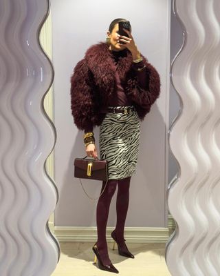 Nina Sandbech in a burgundy faux fur jacket, bag, and tights with a zebra print skirt.