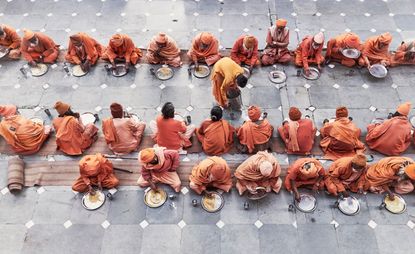 Photo of sadhus dressed in orange sitting on the floor eating from round plates