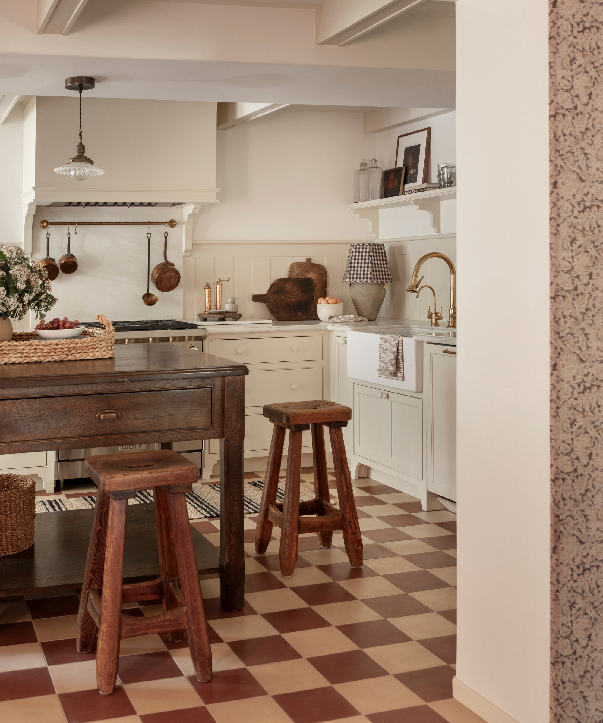 A warm white kitchen with a wood freestanding island and cream and burgundy checkerboard floor tiles