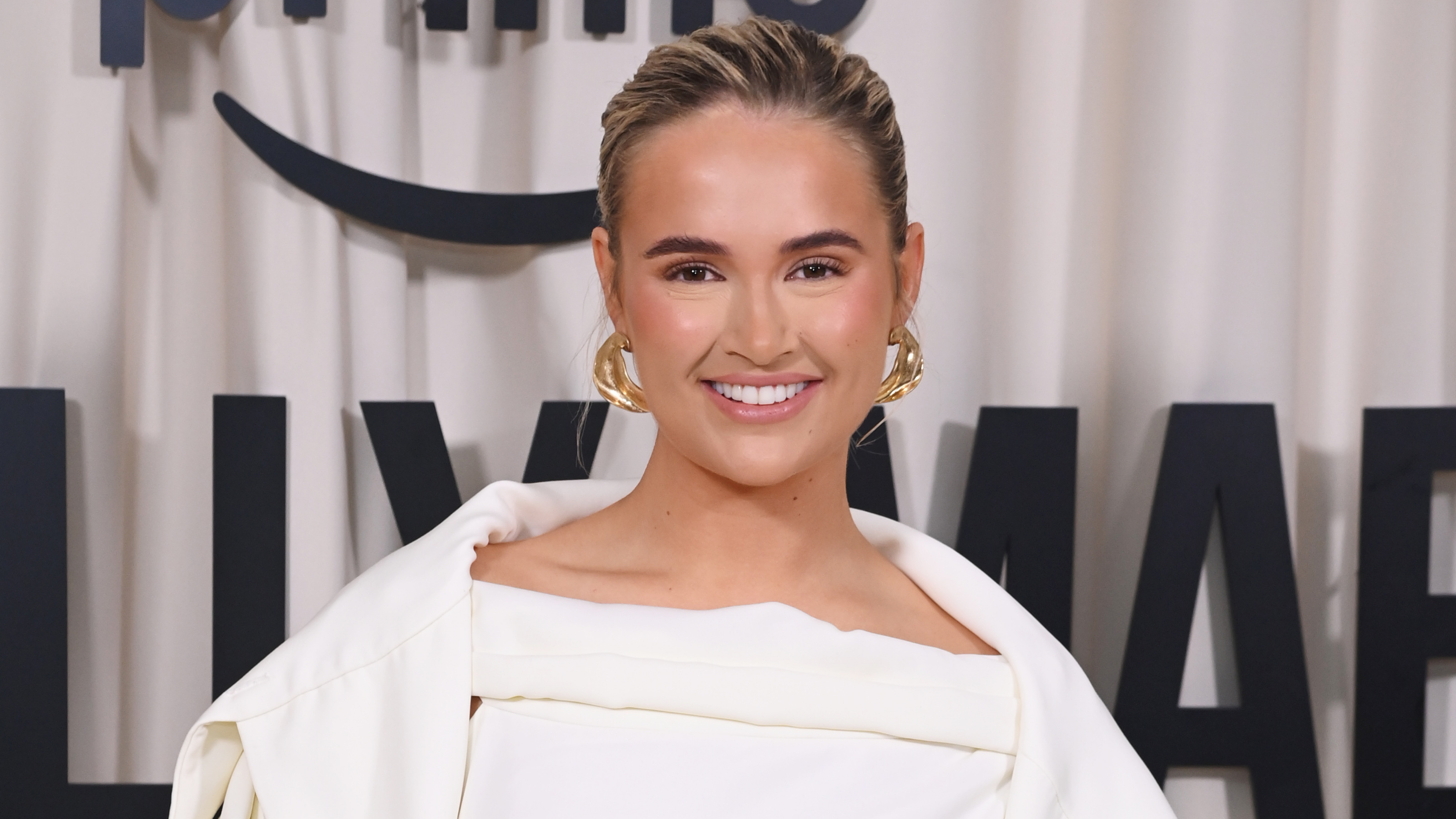 Molly Mae smiling on red carpet wearing white suit.