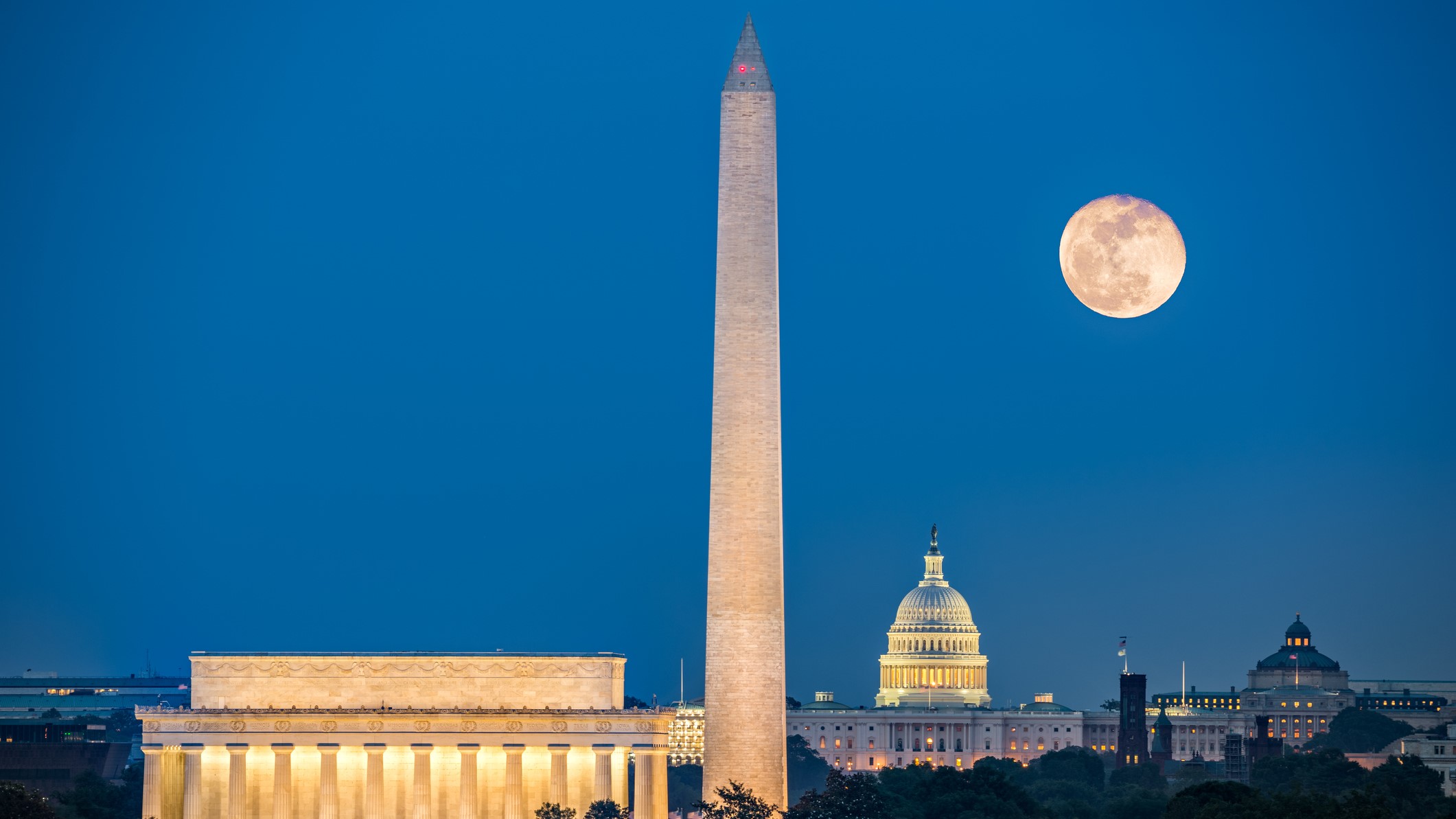 A large moon in sky above the Lincoln Memorial, Washington Monument and Capitol Building in Washington DC.