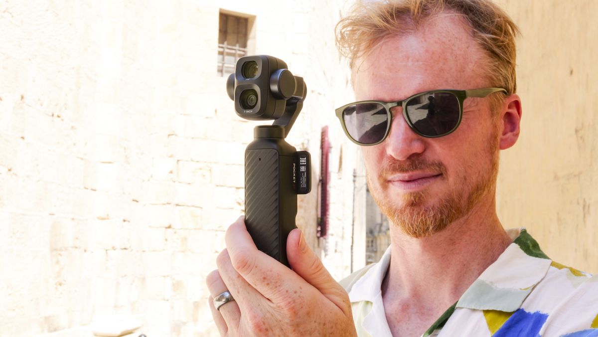 Man in bright summer short and shades, in an old town on a sunny day, holding the DJI Osmo Pocket 4P vlogging camera