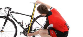 This image shows someone couched down measuring the height of the saddle on a road bike