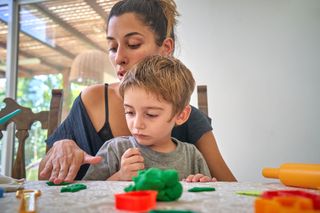 Mother and son sitting at table playing with green clay/playdough