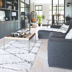 Snug with grey sofa and square coffee table, with built in cabinets opposite, and internal glazed doors leading to a dining area