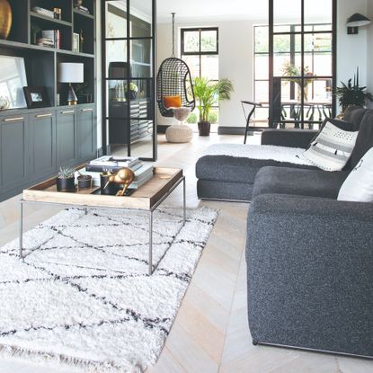 Snug with grey sofa and square coffee table, with built in cabinets opposite, and internal glazed doors leading to a dining area