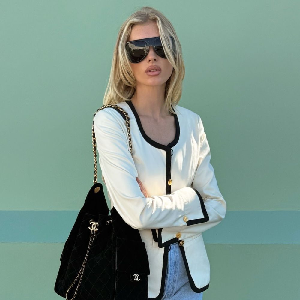 Elsa Hosk wears a white jacket with black trim over light-wash blue jeans with black loafers and a black Chanel shoulder bag.