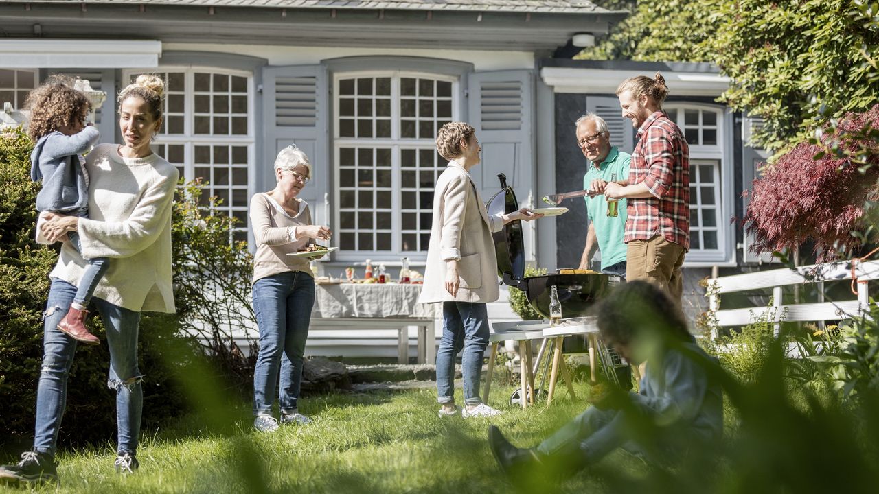 A multigenerational family have a barbecue outside the parents&#039; home.