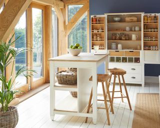A kitchen diner with ivory and light wood kitchen island, wooden oak bar stools and ivory/light wood larder