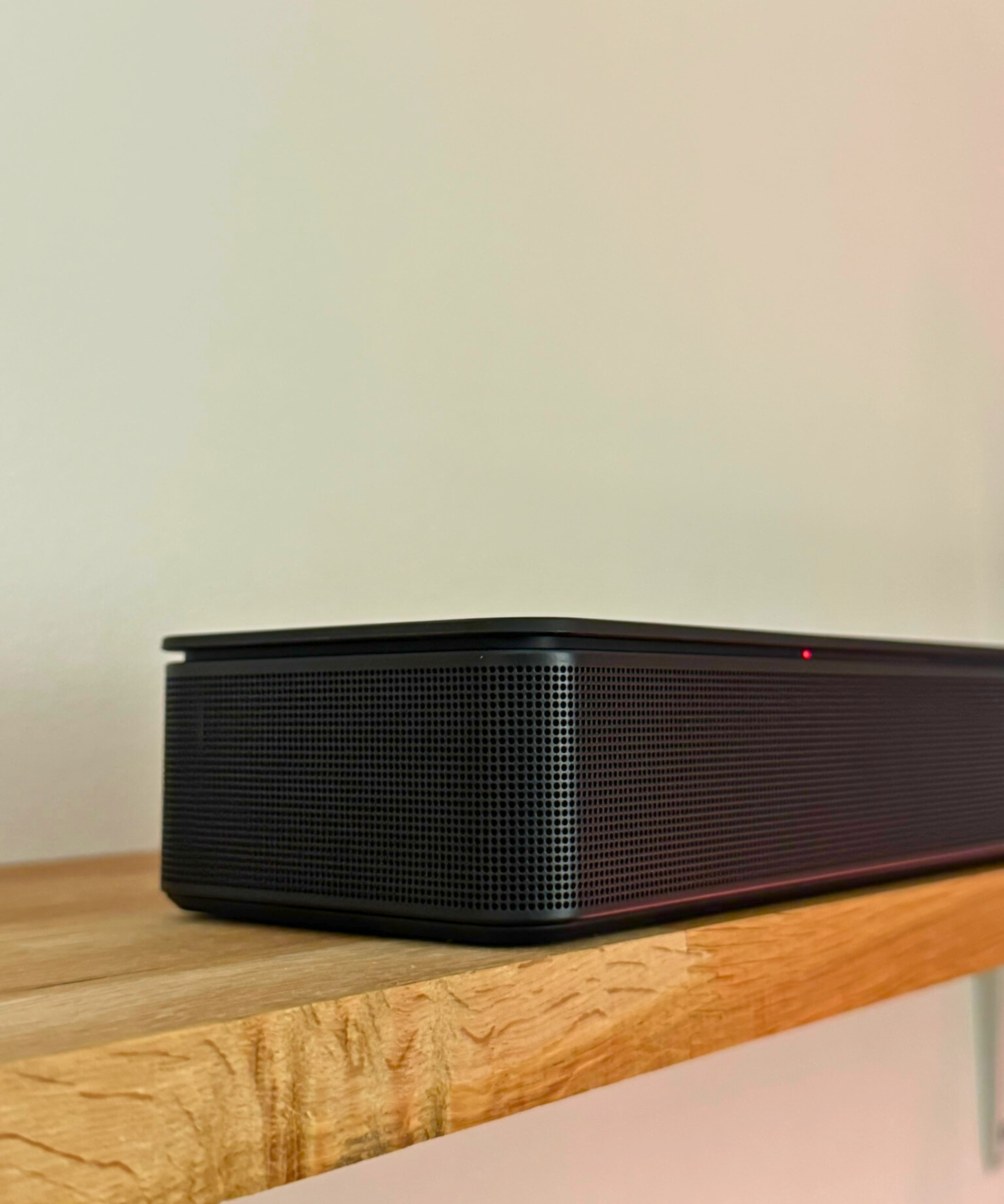 Corner of the Bose Smart Soundbar on wooden shelf in front of white wall.