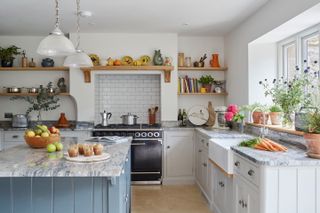 kitchen with blue freestanding island with marble worktops, white kitchen cabinetry with bulter's sink and black stove