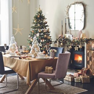 A dining room decorated for Christmas. A fire is lit and golden stars hang from the ceiling above a decorated table