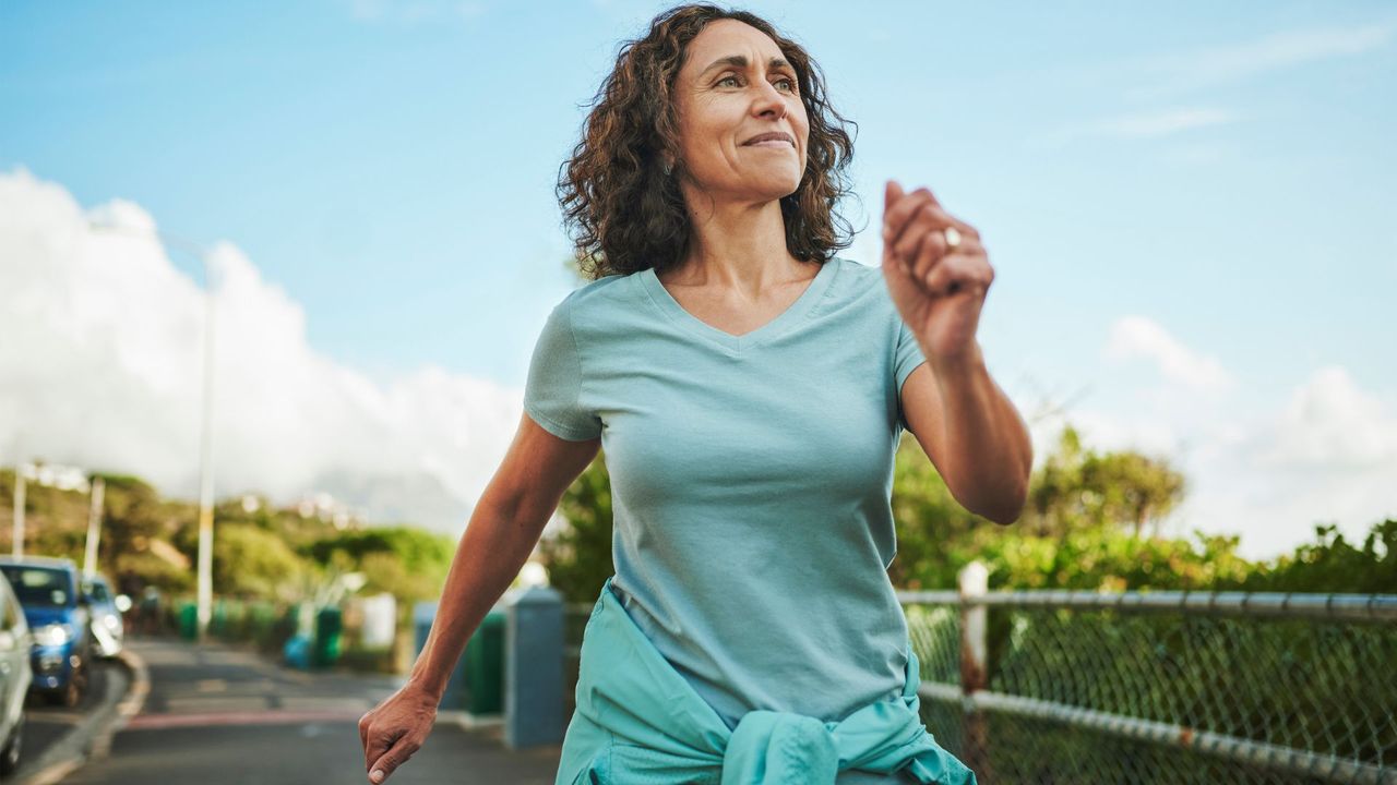 Woman walking with arms swinging outside in the summer sunshine, representing why you may need to take vitamin D in summer