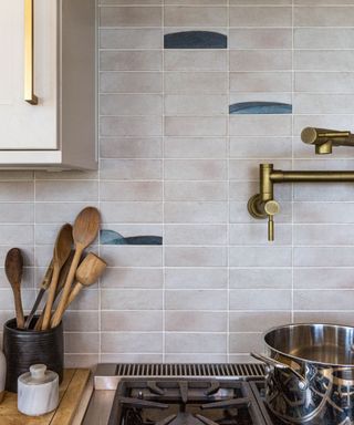 A tile backsplash in a kitchen with patina metal finishes