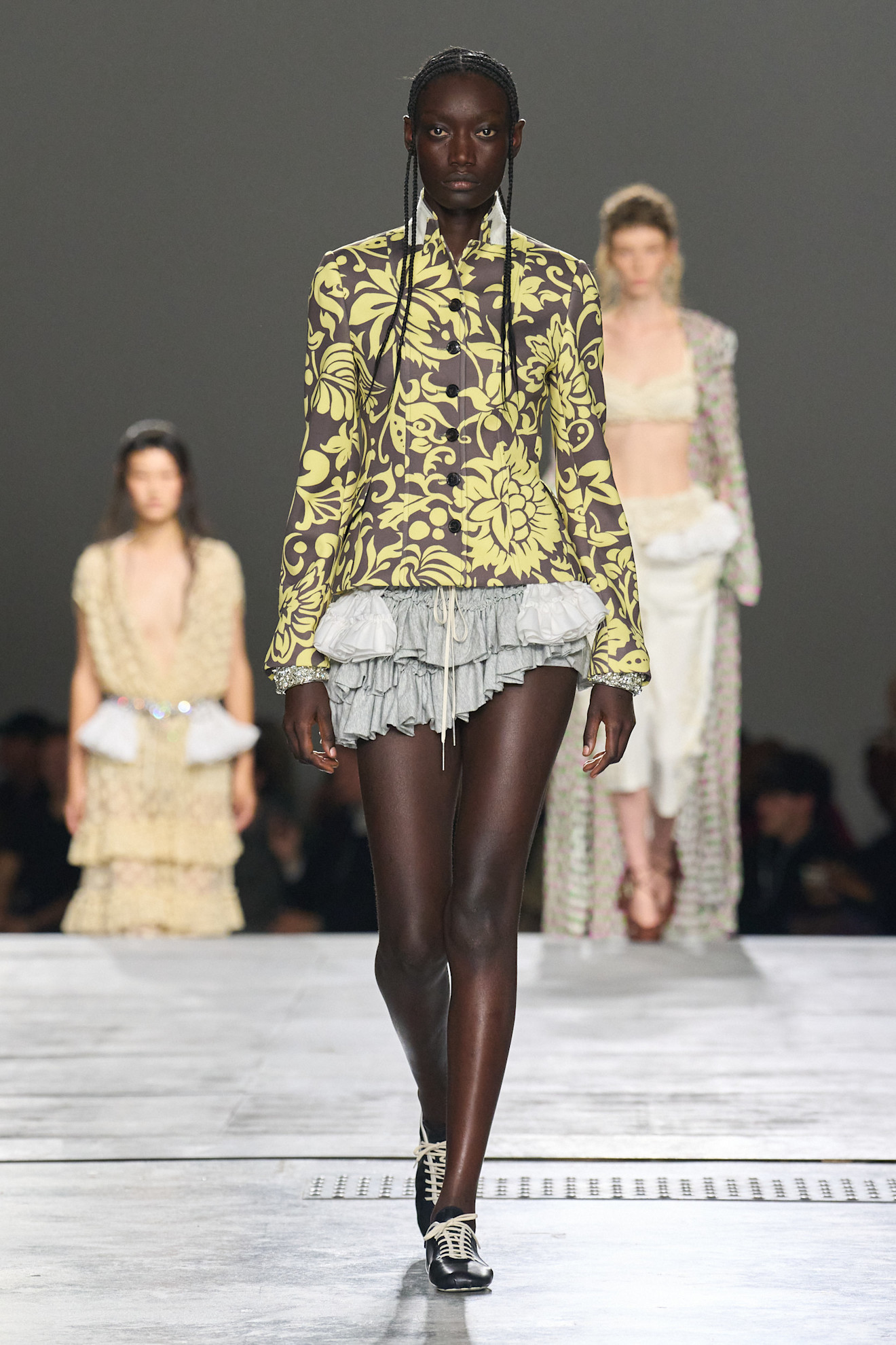 A model at the spring/summer 2026 Dries Van Noten show wearing a brocade printed jacket with a gray, draped miniskirt.
