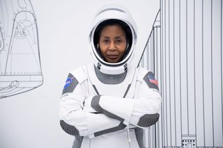 stephanie wilson in a spacesuit with arms crossed, in front of a mural depicting a rocket