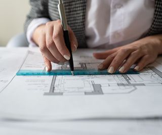 woman's hand holding compass over set of architectural plans