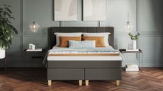 Emma mattress deals premium mattress on dark grey bed with blue walls and orange cushions 
