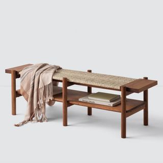 A wooden bench with a woven center and a blanket thrown across it, for the best sustainable brands.