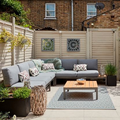 A garden with a light wood fence and a corner outdoor sofa with grey cushions and a wooden coffee table