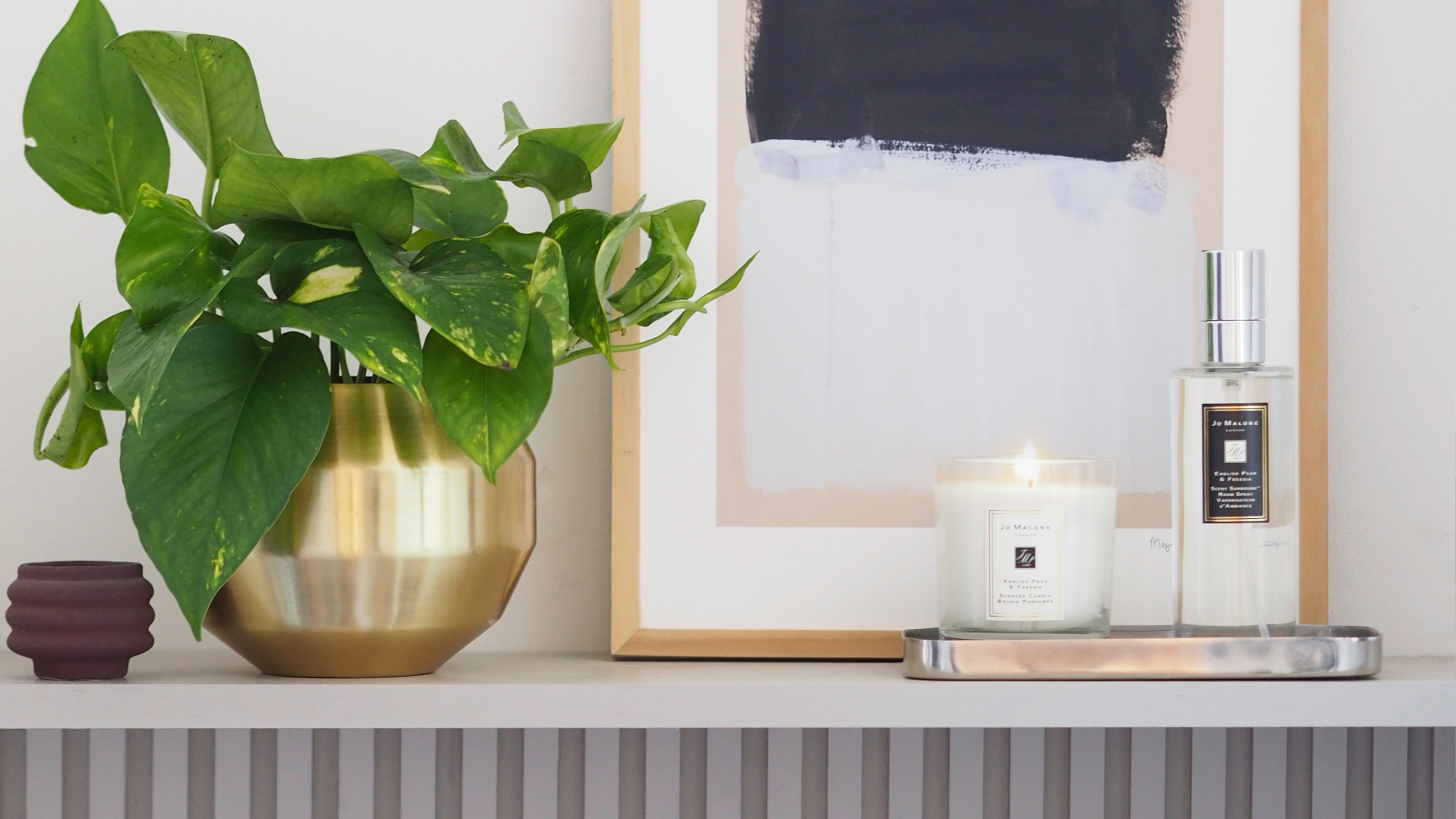 a shelf with a plant, picture frame, and jo malone candle and room spray