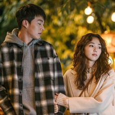 a girl holds a boy's arm while walking on a date in a still from a korean romance movie