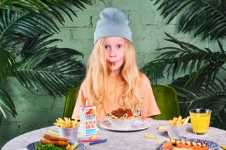 A young girl sat at a table surrounded by kid's meals