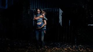 Shirin bär sin son Lucas utanför deras hus i skräckfilmen Andra sidan
