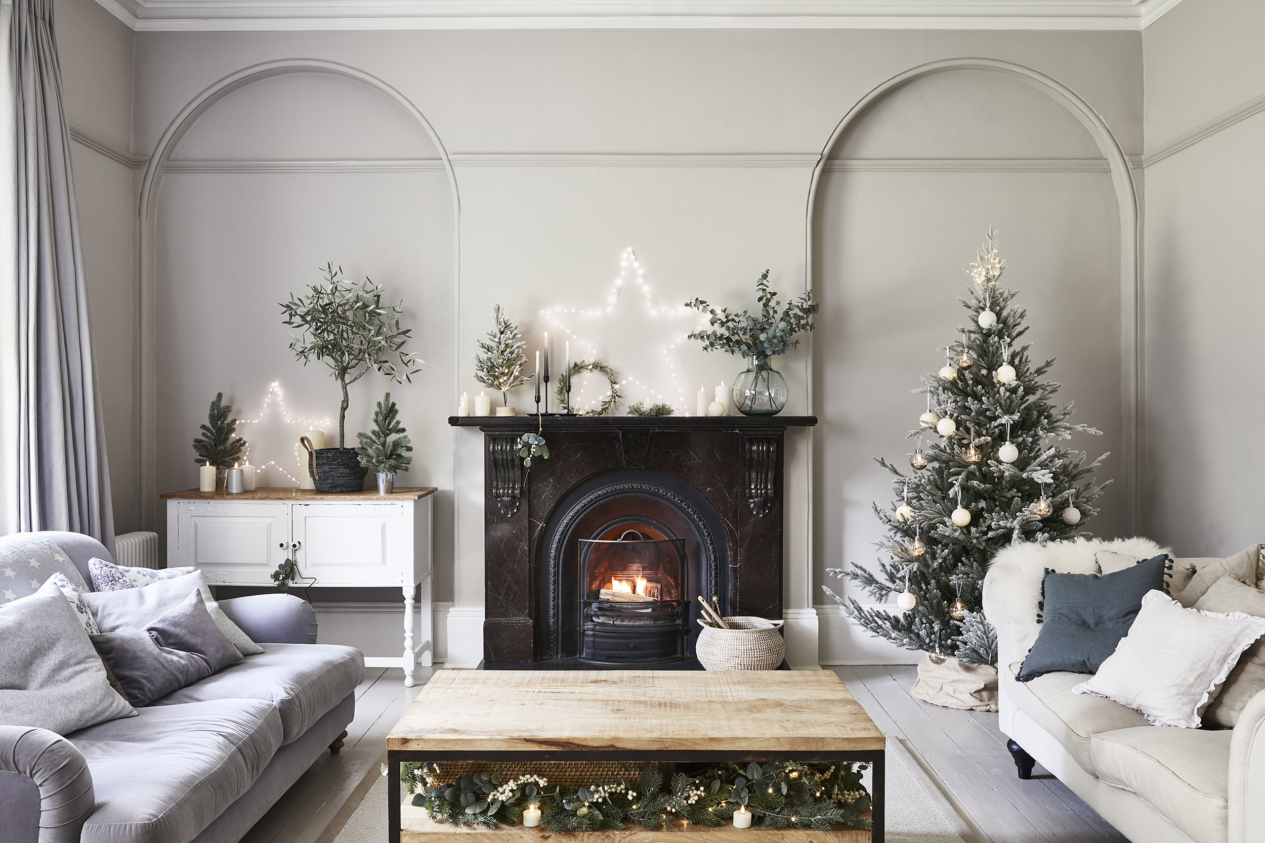 A living room with Christmas fairy lights, fireplace and two arched wall alcoves