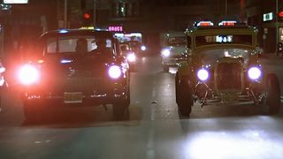Two hot rod cars drive down the street in American Graffiti