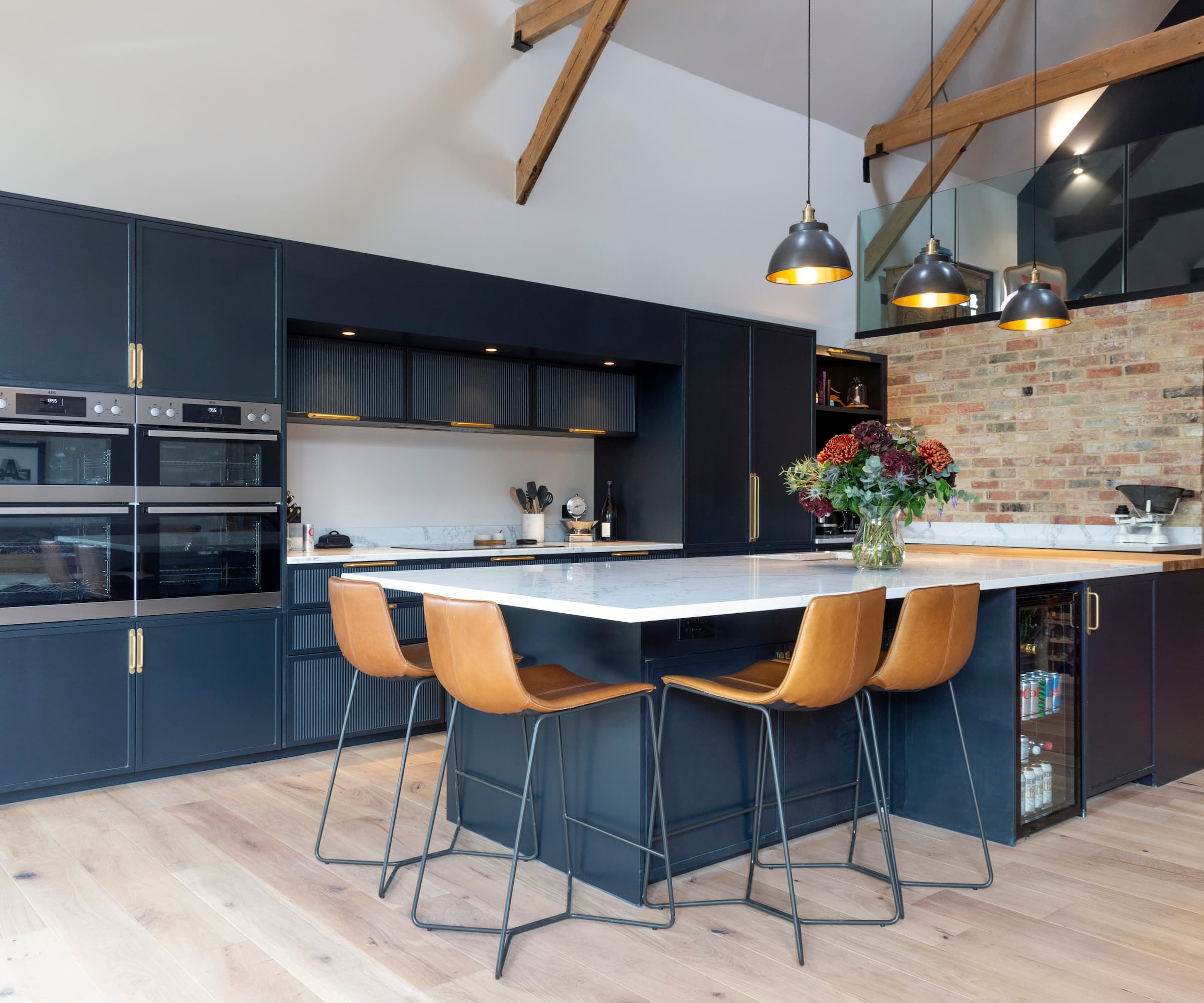 A navy blue kitchen with a white porcelain kitchen island top and four small chairs, all next to a brick wall with overhead lamps