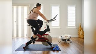 Check out the best exercise bikes on sale. Shown here, a young mother on an exercise bike.