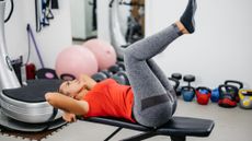 Woman lying on a workout bench in a gym with raised legs