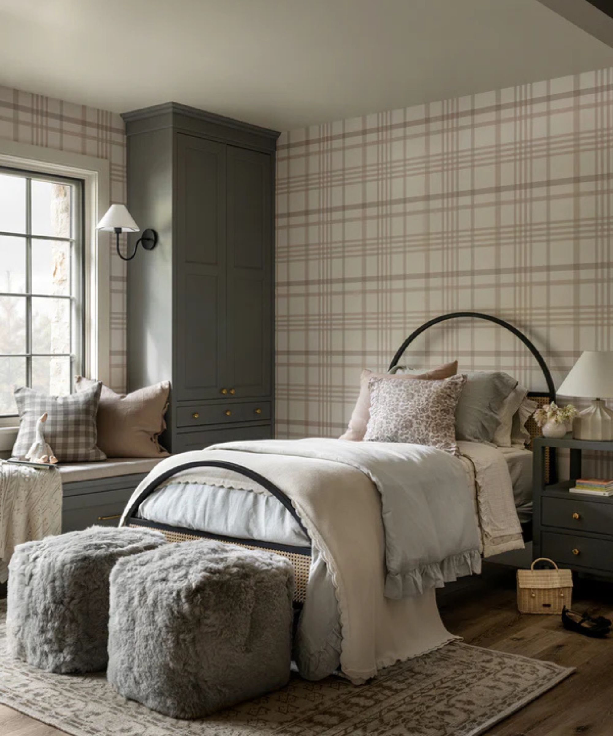 A large bedroom with plaid wallpaper, a black, arched bed frame, and faux fur footstools at the end of the bed
