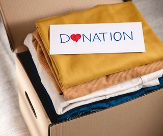 A cardboard box full of folded clothes with a donation sign on top