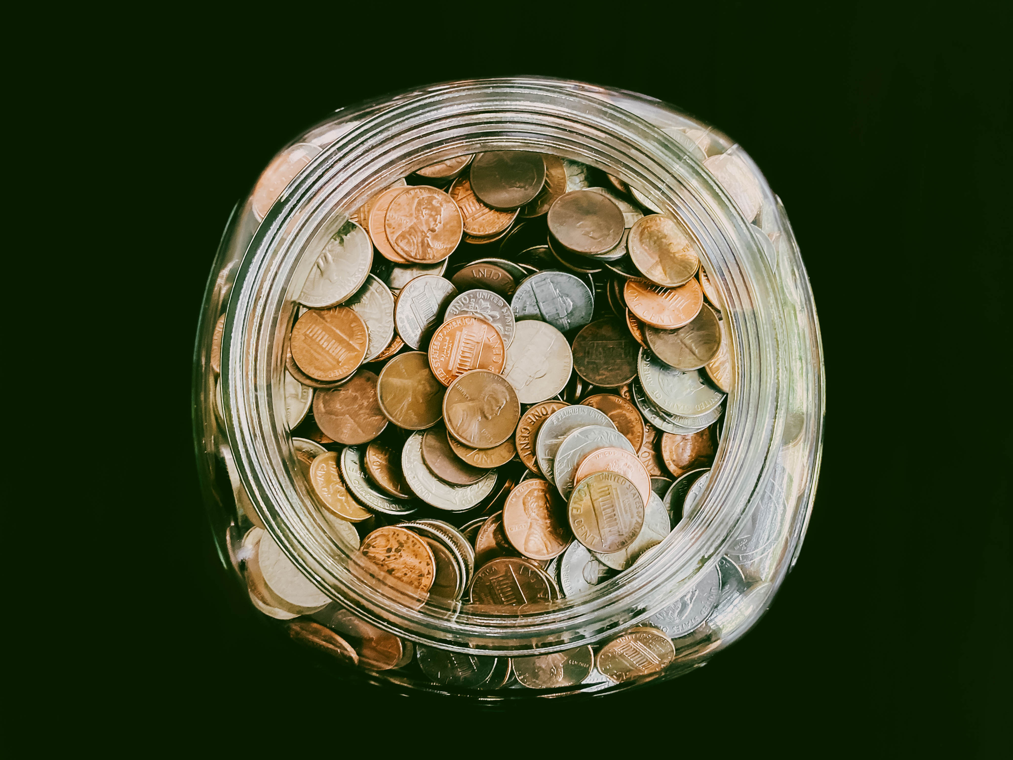 High angle view of glass jar filled with US coins on dark background