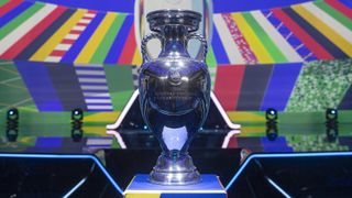 The Euro 2024 trophy on a pedestal in front of some colorful signage