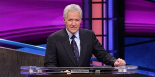 Alex Trebek smiling at his desk on the set of Jeopardy!