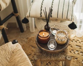 Wicker furniture with eco materials, handicraft cushions, aroma reed diffuser, burning candles and textile at boho chic interior. Hygge and aromatherapy concept. Cozy winter or autumn time.