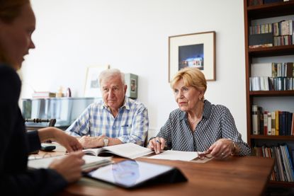 An older couple meets with a financial adviser, looking concerned. 