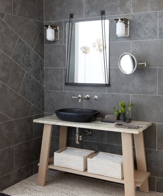 Dark gray wall tiles with white grouting and a wooden sink stand