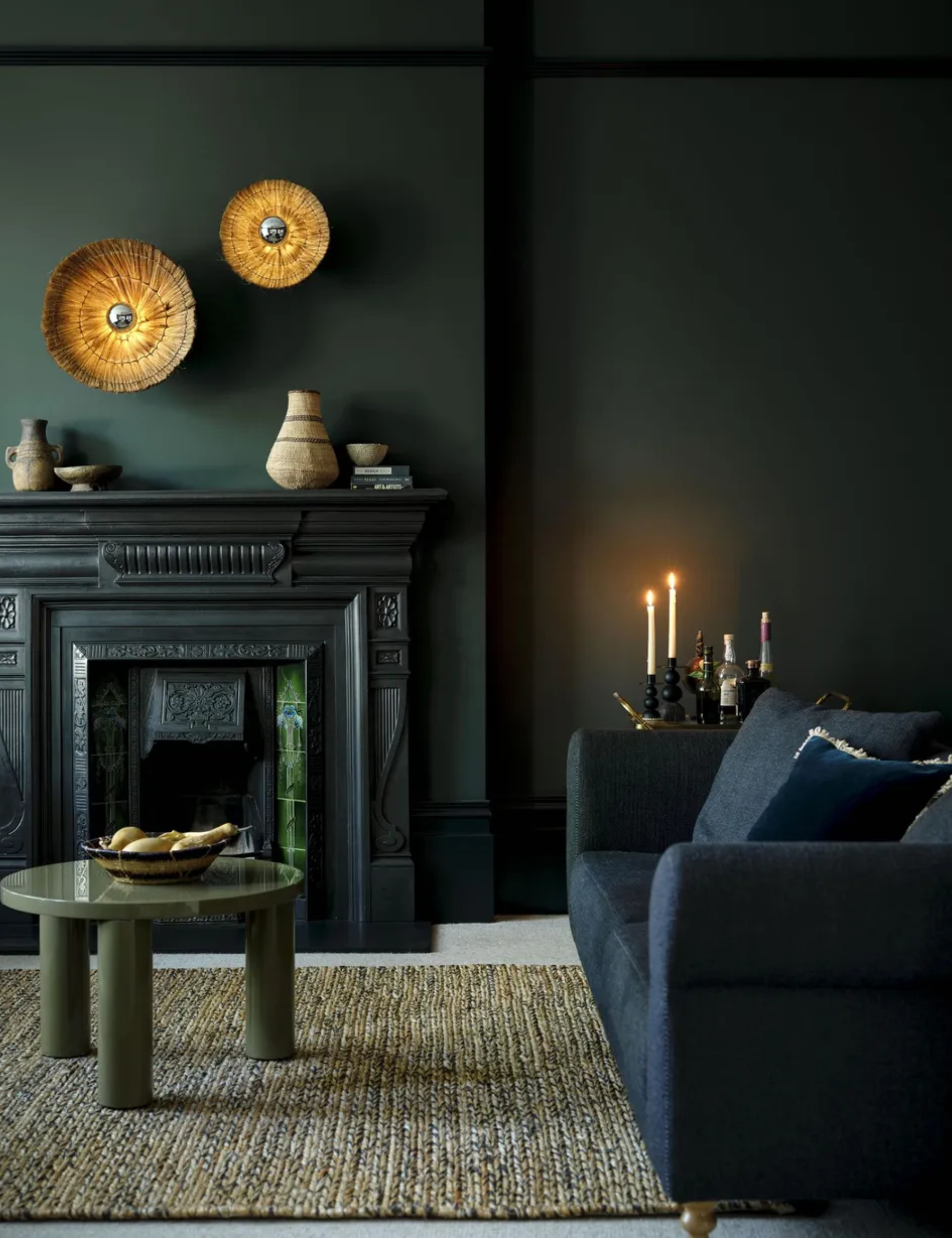 Moody dark coloured living room with dark blue sofa, green shiny coffee table, gold wall art and fireplace